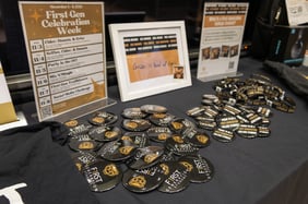A table with a black cloth and Oakland First Buttons with a bear icon on them next to table displays with the celebration schedule.