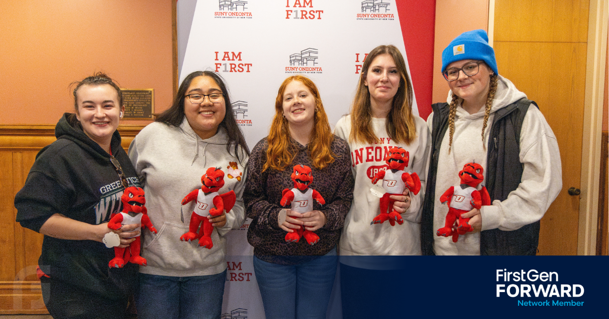 Group of students holding Red Dragon plush mascots in front of an “I Am First” SUNY Oneonta backdrop